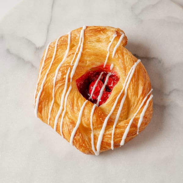 A golden-brown pastry with white icing drizzle and a cherry filling center on a marble surface.