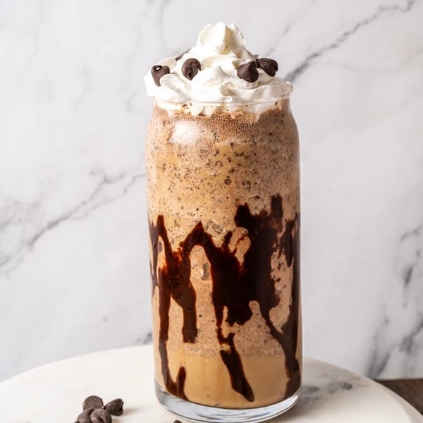 Chocolate chip frappe with whipped cream and chocolate drizzle in a tall glass.