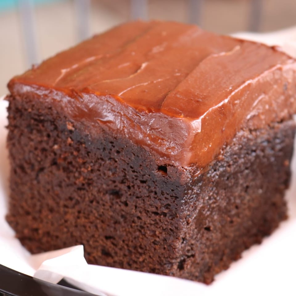 A close-up of a square chocolate brownie with a thick layer of chocolate frosting.